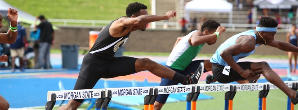 Male hurdlers stretch over the hurdles in a race at the 2019 State Track and Field Meets.