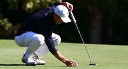 A male golfer prepares to line up a putt during the State Golf Tournament.