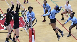 A female volleyball prepares to spike the ball as two defending blockers move into position at the net during the 2018 State Semifinals.