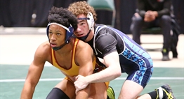 Two male wrestlers are poised to restart as they await the referee's signal at the 2019 State Tournament.