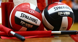 Two three-paneled red and black Spalding volleyballs and endline officials flags sitting on the head official's stand.