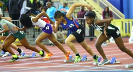 A group of female sprinters burst from the starting blocks in a 2016 State Indoor Meet race.