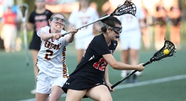 A female defender strains to check an offensive player cradling the ball in the 2018 State Lacrosse Finals.
