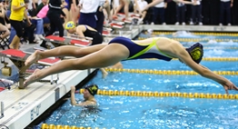 A female swimmer dives into the pool during a State Meet relay race in 2016.