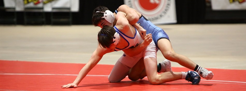 A male wrestler controls his opponent on the mat from behind during the 2019 State Tournament.