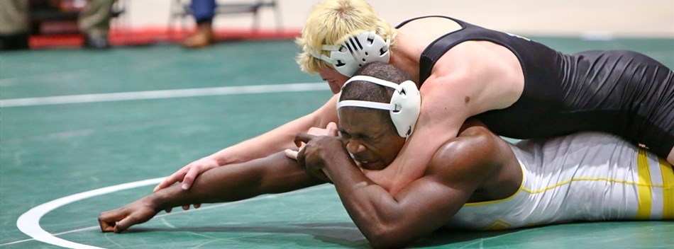A male wrestler controls his opponent face down on the mat at the 2019 Class 2A/1A State Tournament.